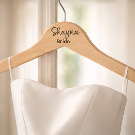 White wedding dress on a wooden hanger with 'Shayna Bride' engraved.