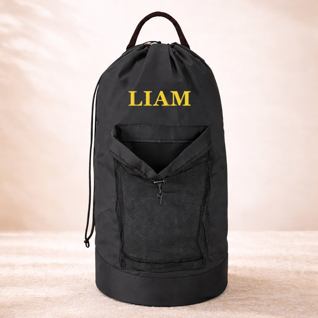 Black drawstring bag with 'LIAM' embroidered on it against a beige background