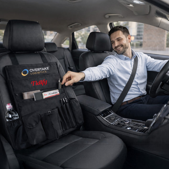 Man in a car with a black organizer on the back seat, featuring 'Overtake Logistics' and 'Tidify' branding.