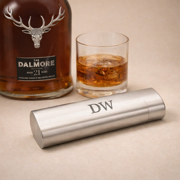 Dalmore whiskey bottle with a glass of whiskey and a silver tumbler on a beige surface