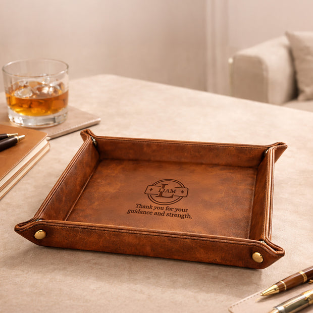 Brown leather tray with engraved text on a table with a glass of whiskey and pen.