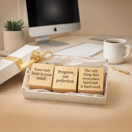 Wooden blocks with motivational phrases in a gift box on a desk with a computer and coffee cup.