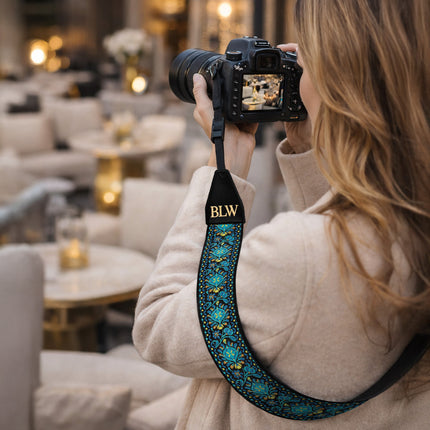 Person holding a camera with a decorative strap in an indoor setting