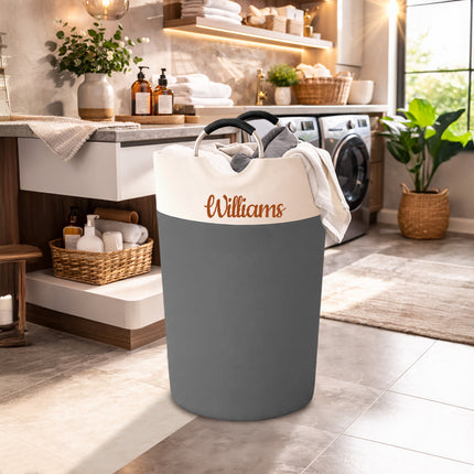 Gray laundry basket with 'Williams' branding in a bright laundry room.