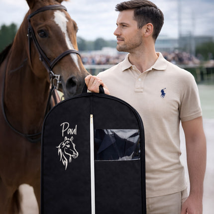Man holding a black garment bag with a horse design and 'Paul' text, standing next to a brown horse.