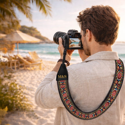 Man taking a photo on a beach with a camera featuring an 'M&S' strap.