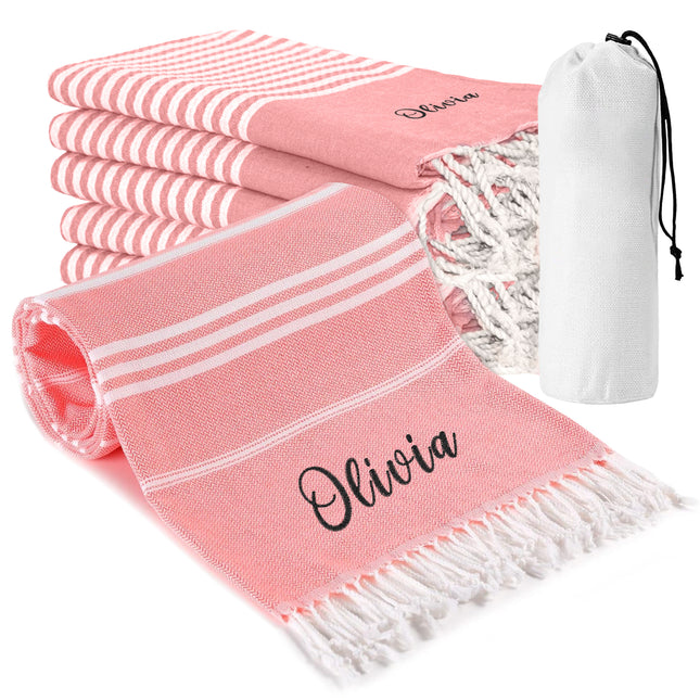 A set of pink and white striped beach towels with custom names embroidered on them, accompanied by a white drawstring storage bag.