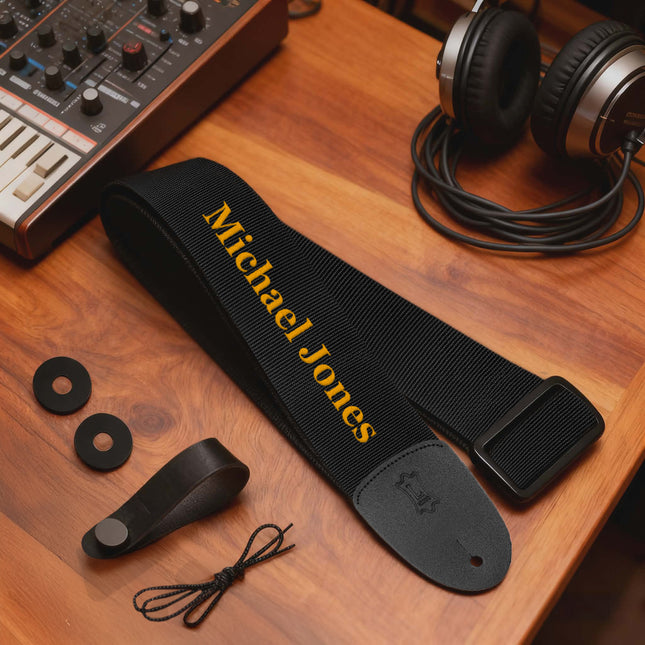 Black guitar strap with 'Michael Jones' branding on a wooden surface with headphones and equipment.