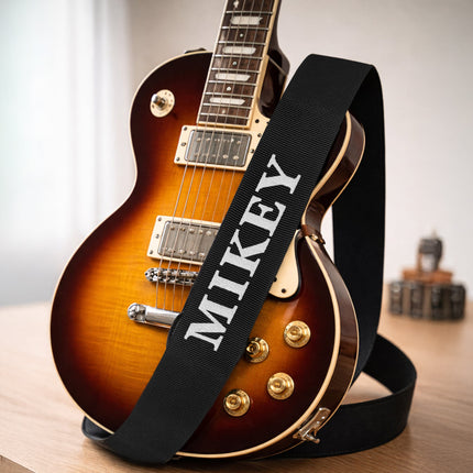 Electric guitar with a black strap labeled 'MIKEY' on a wooden surface.