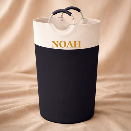 Black and white laundry basket with 'NOAH' branding on a beige fabric background