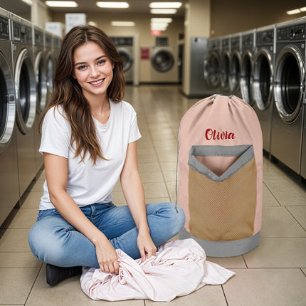 A pink personalized laundry bag with a mesh pocket, hanging shoulder strap, and custom text 'Olivia' printed on the front
