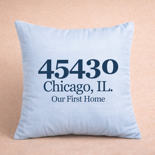Light blue pillow with black text '45430 Chicago, IL. Our First Home' on a beige background