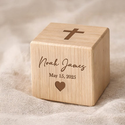 Wooden cube with engraved name, date, and cross symbol on a textured beige background