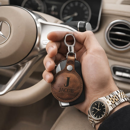 Hand holding a car key with a leather case featuring 'JACOB' inside a car.