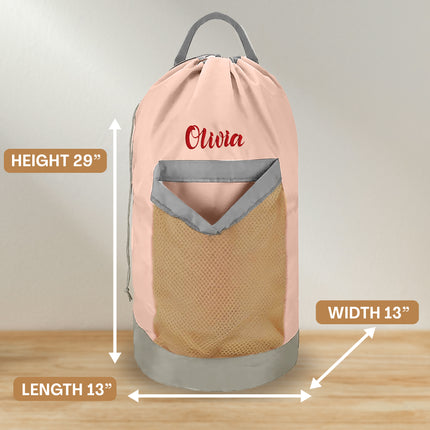 A pink personalized laundry bag with a mesh pocket, hanging shoulder strap, and custom text 'Olivia' printed on the front