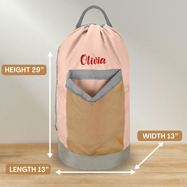 A pink personalized laundry bag with a mesh pocket, hanging shoulder strap, and custom text 'Olivia' printed on the front