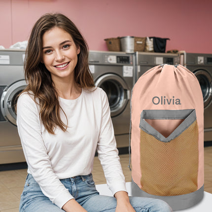 A pink personalized laundry bag with a mesh pocket, hanging shoulder strap, and custom text 'Olivia' printed on the front