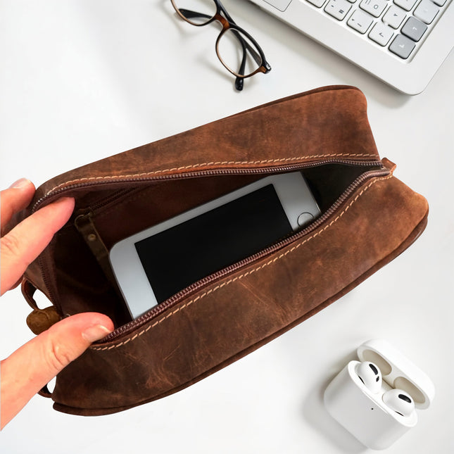 Brown leather pouch containing a smartphone, with a hand holding it open on a white surface.