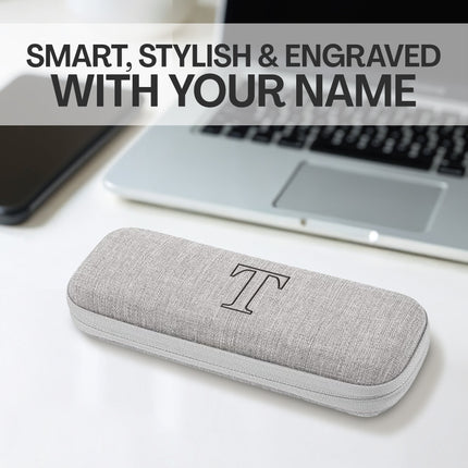 Gray glasses case with a monogram 'T' on a desk with a laptop and phone.