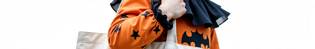 Child in Halloween costume holding a tote bag with a pumpkin design.