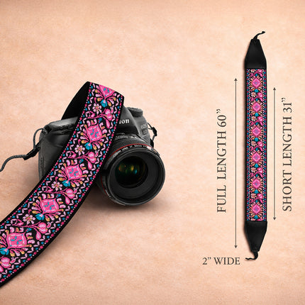 Camera strap with pink floral pattern next to a DSLR camera on a beige background